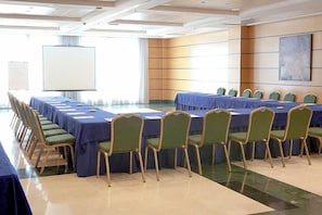 Un salón de conferencias con una larga mesa y sillas, una pizarra y un amplio ventanal.