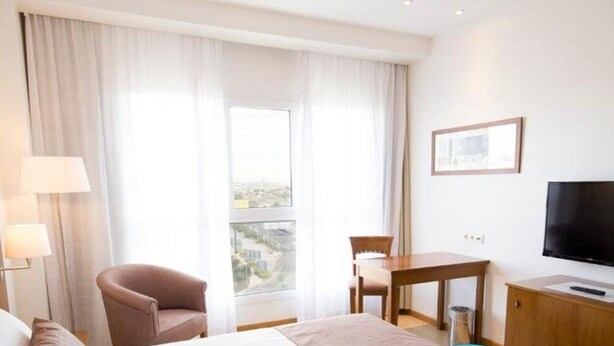 A hotel room with a bed, a chair, a desk, a TV, and a window with curtains. - Hotel Albufera (Alfafar)