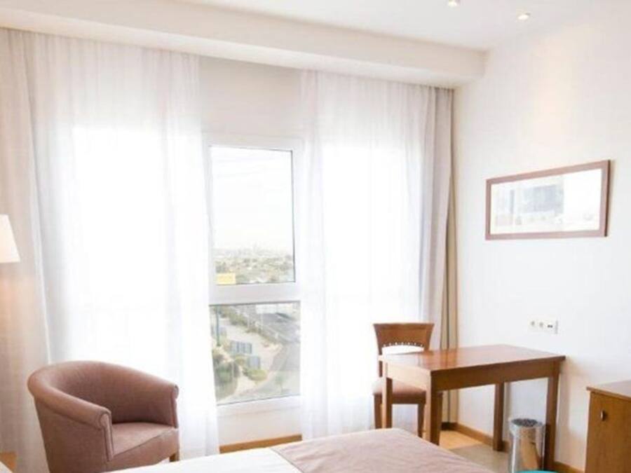 A hotel room with a bed, a chair, a desk, a TV, and a window with curtains.