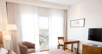 A hotel room with a bed, a chair, a desk, a TV, and a window with curtains.