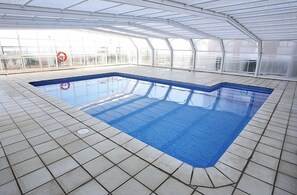 Una piscina interior con suelo de baldosas y techo de cristal.