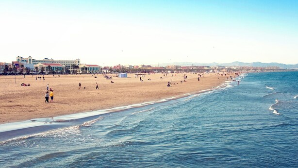 A wide beach with a clear sky, a few people, and buildings in the background. - Hotel Albufera (Alfafar)