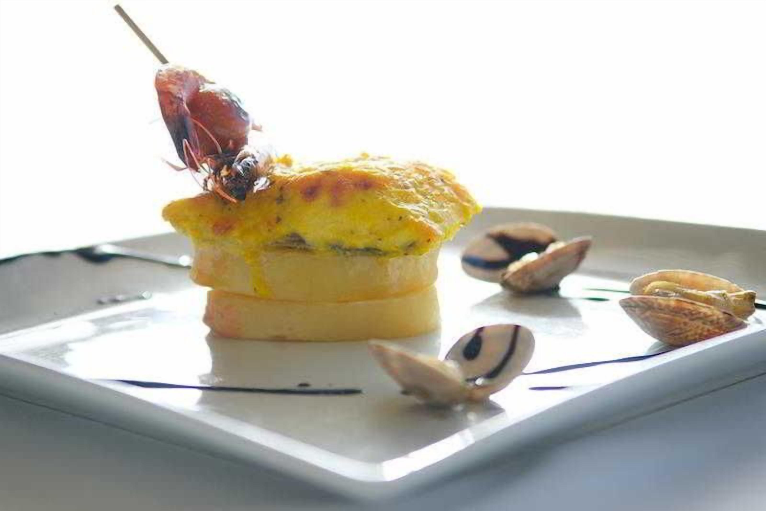 A dish with a lobster tail on a skewer, a baked item, and pistachio shells on a white plate.