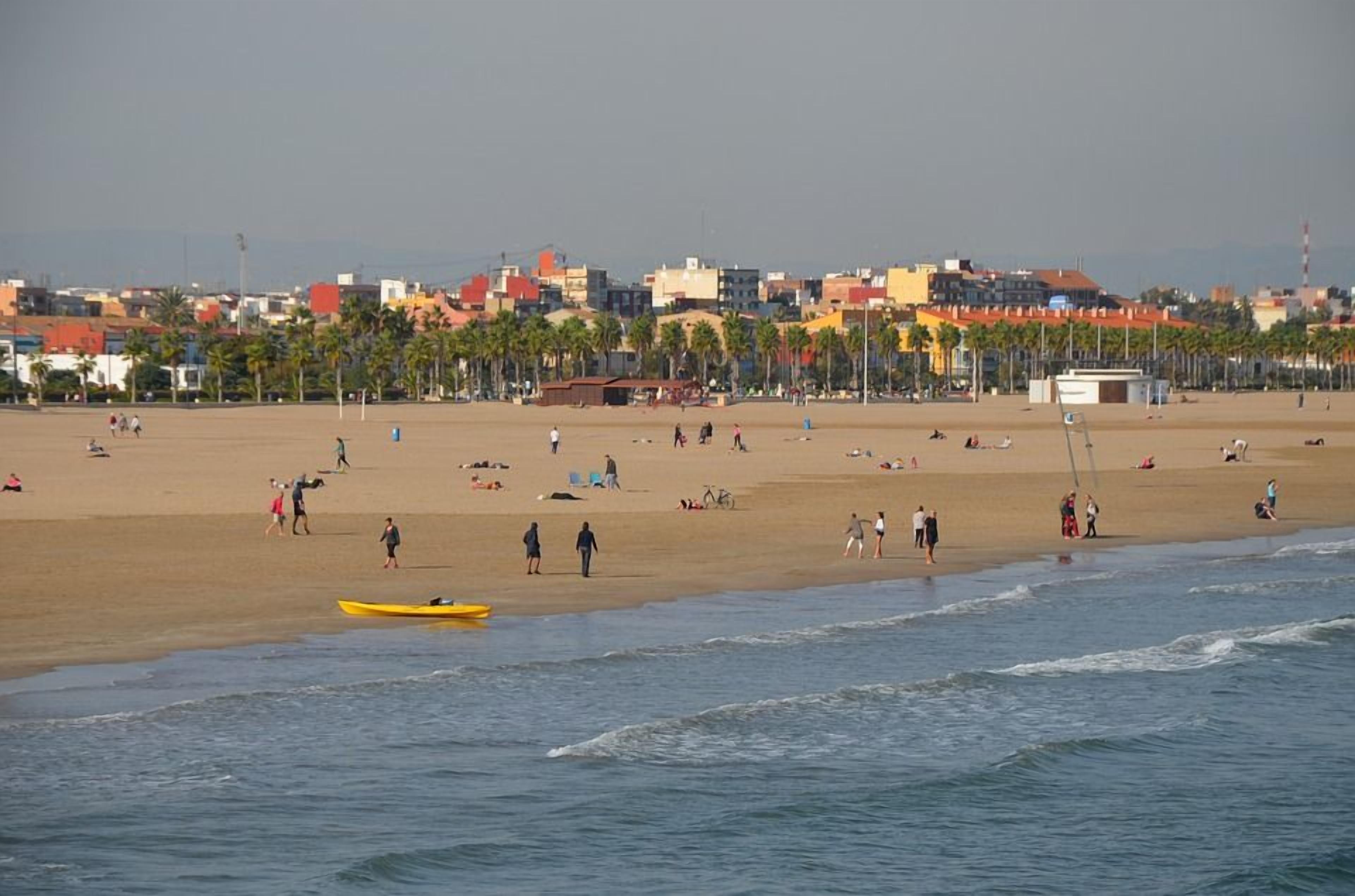Una playa con gente, un bote amarillo y edificios al fondo.