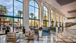 A spacious lobby with large arched windows, a seating area with sofas and chairs, and a staircase leading to an upper level. - Barceló Punta Umbría Mar (Punta Umbría)