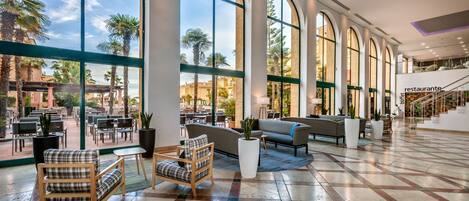 A spacious lobby with large arched windows, a seating area with sofas and chairs, and a staircase leading to an upper level.