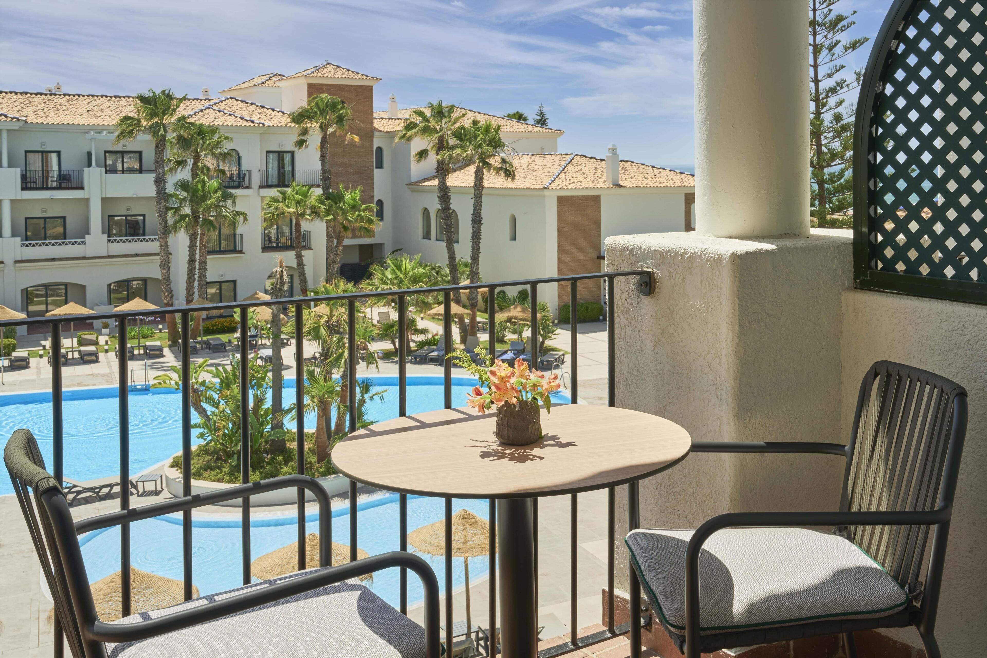 Un balcon donnant sur une piscine, des palmiers et un bâtiment d’hôtel.