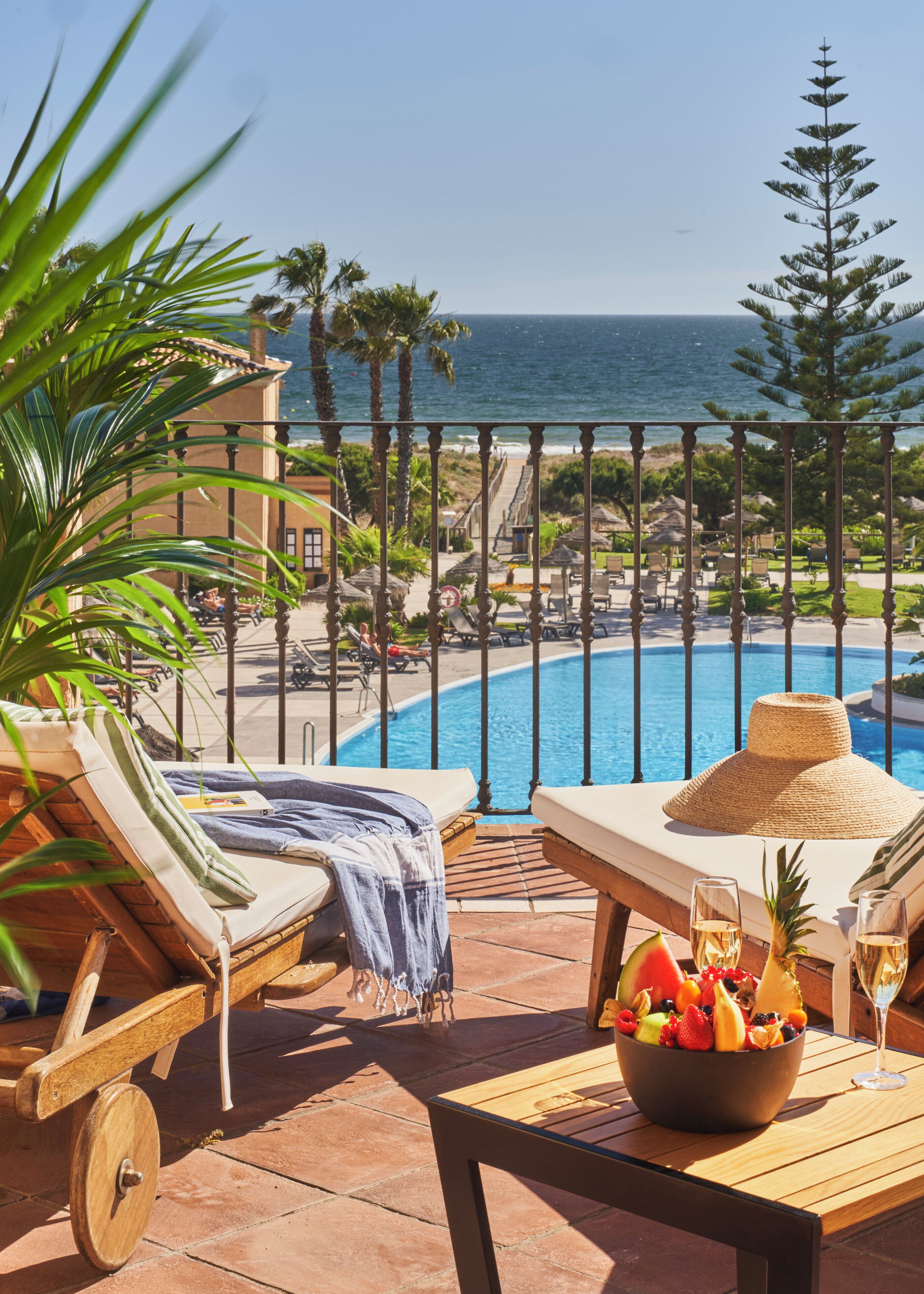 Un área junto a la piscina con sillones de descanso, una mesa con frutas y bebidas, y vista al océano.