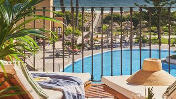 Un área junto a la piscina con sillones de descanso, una mesa con frutas y bebidas, y vista al océano.