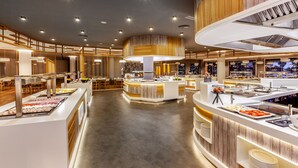 A modern hotel lobby with multiple buffet stations, wooden accents, and a spacious layout. - Barceló Punta Umbría Mar (Punta Umbría)