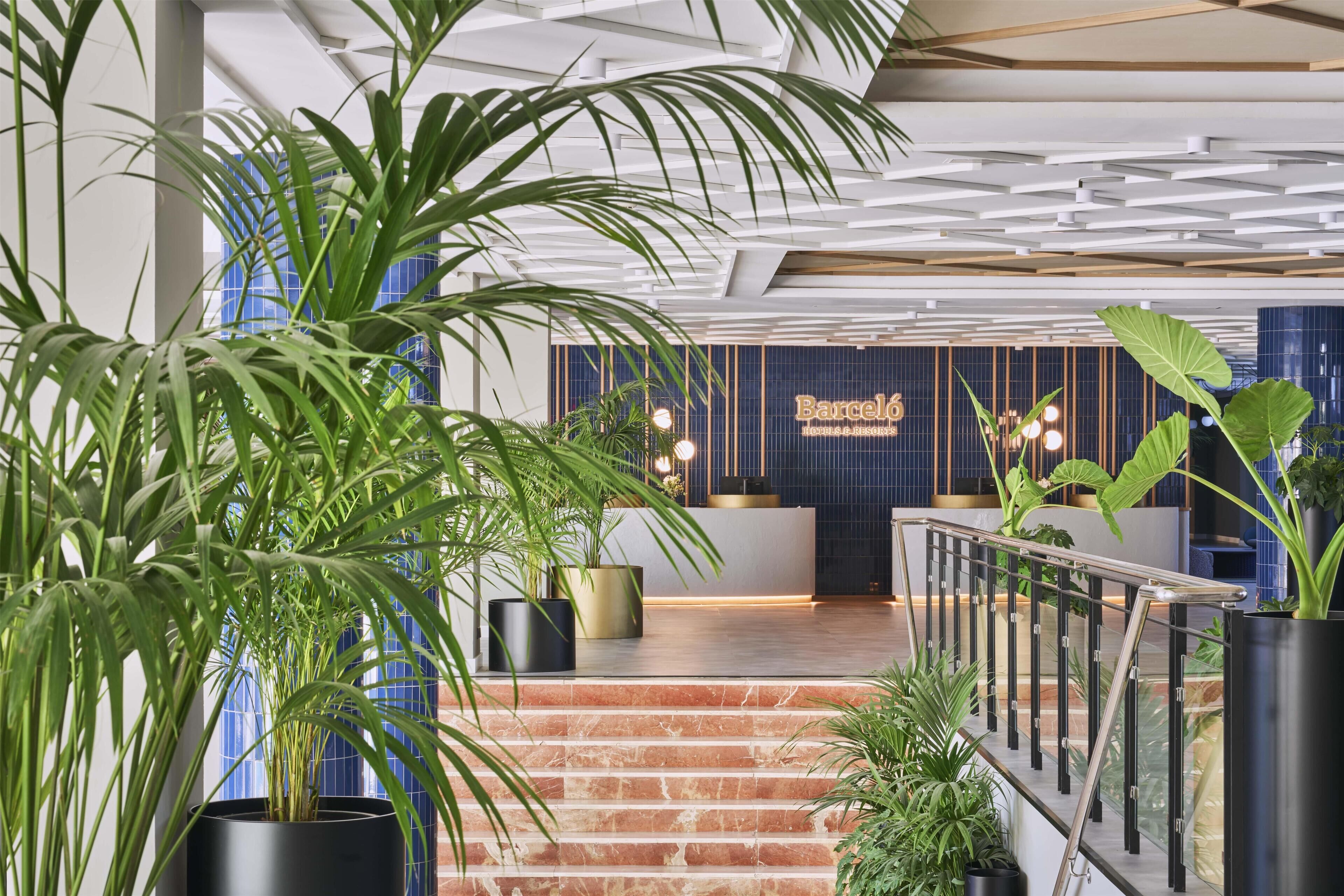Eine moderne Hotelhalle mit einer Rezeption, einer Treppe und Blumentöpfen.