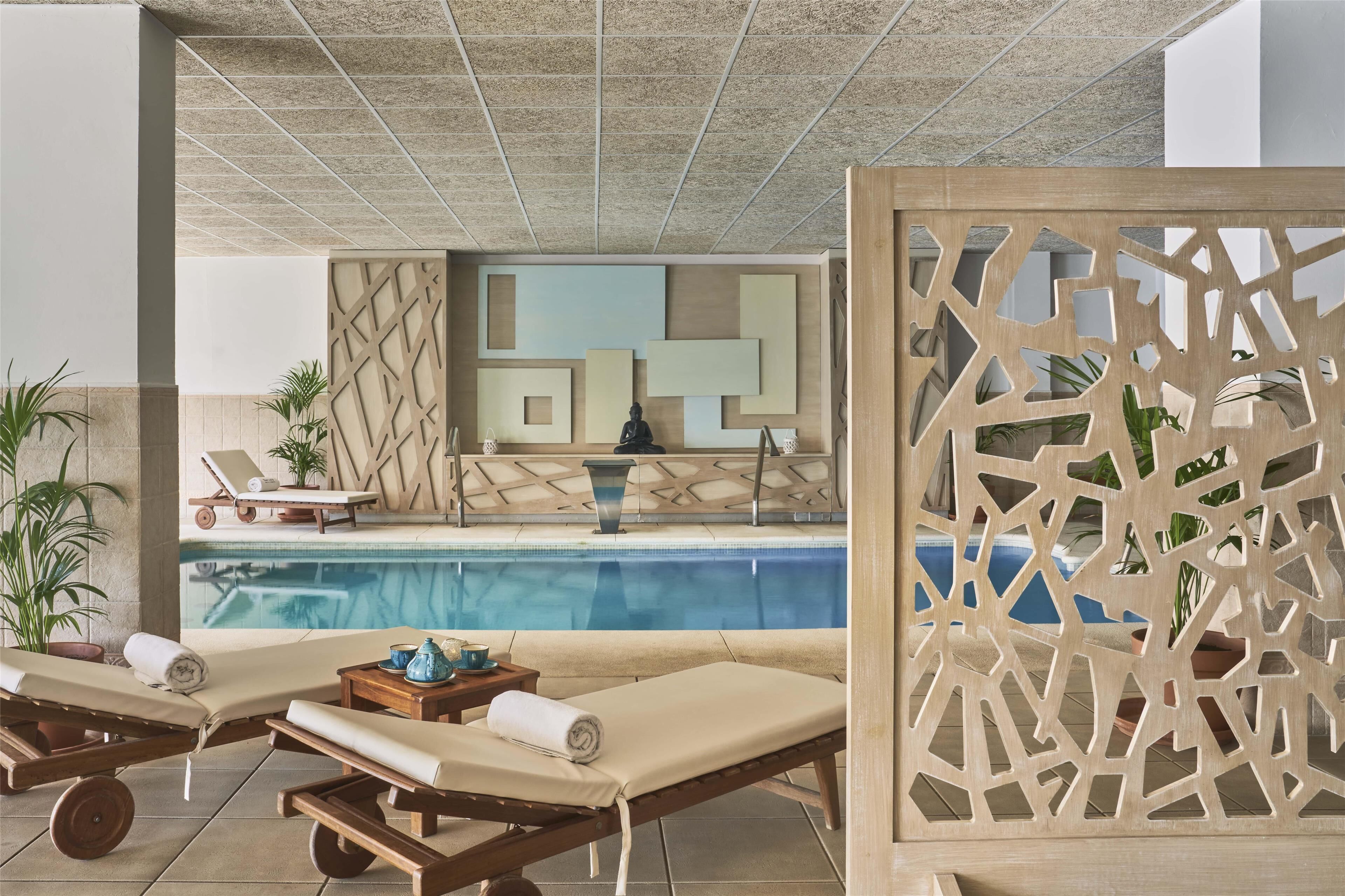 Un área junto a la piscina con sillas de descanso, un muro decorativo y una vista despejada del estanque.
