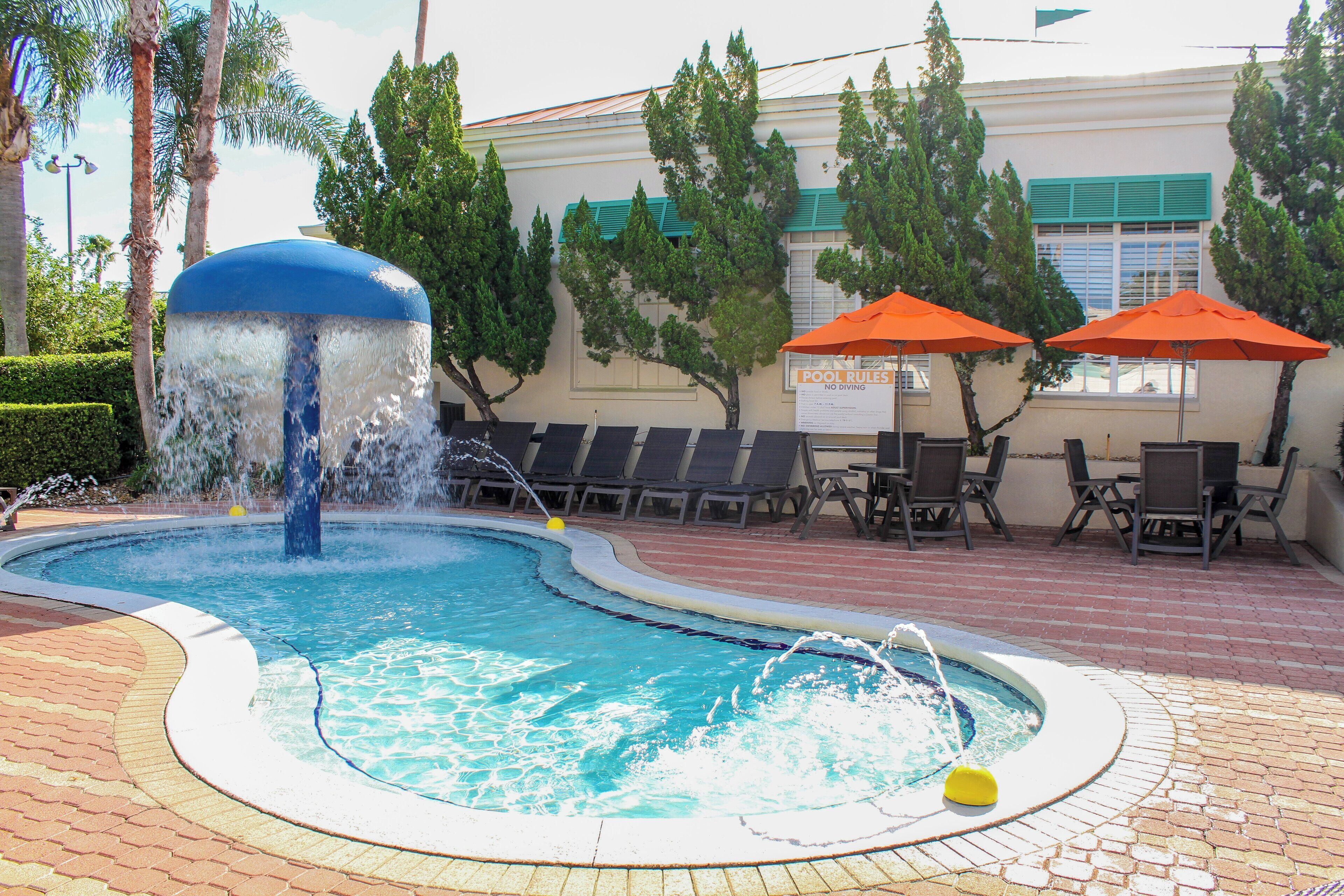 Una piscina con fuente de agua, rodeada de sillones de descanso y sombrillas.
