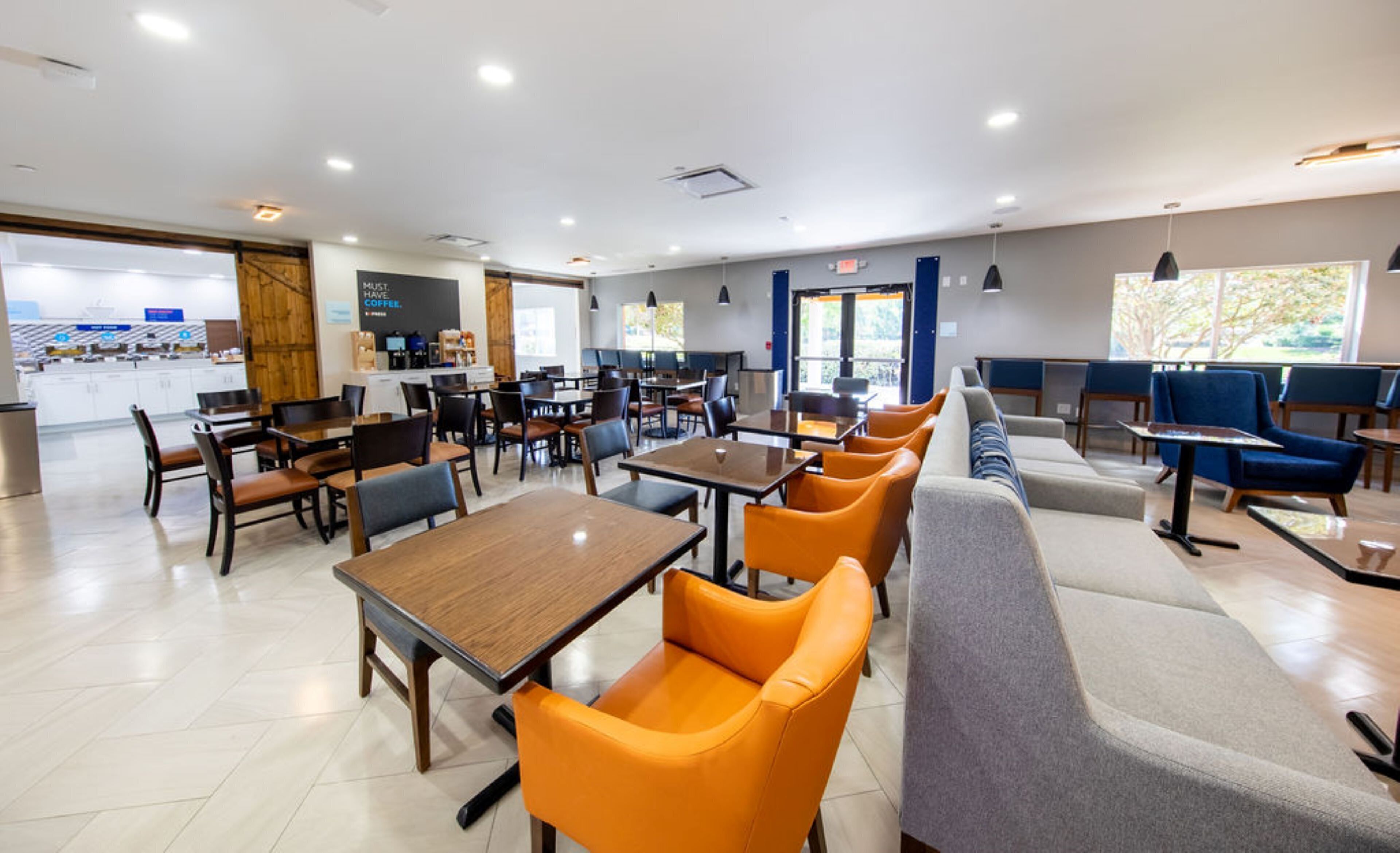 A modern cafe with wooden tables, orange chairs, and a seating area with blue sofas.