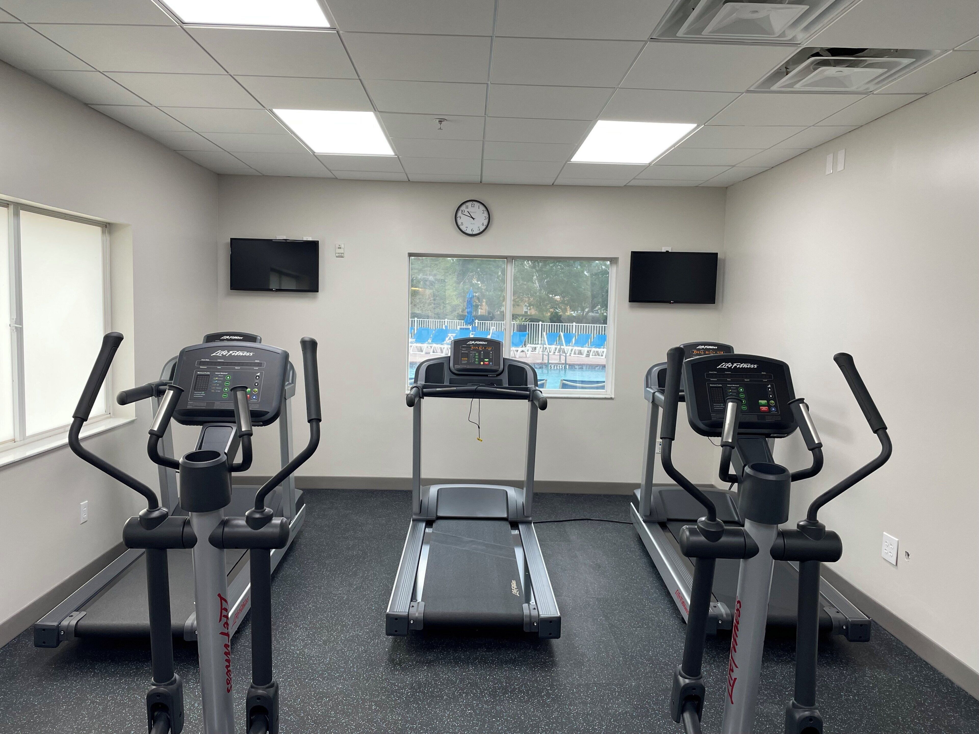 Ett gym med tre löpband, en motionscykel och en väggklocka.