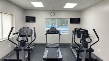 Un gimnasio con tres cintas de correr, una bicicleta estática y un reloj de pared.