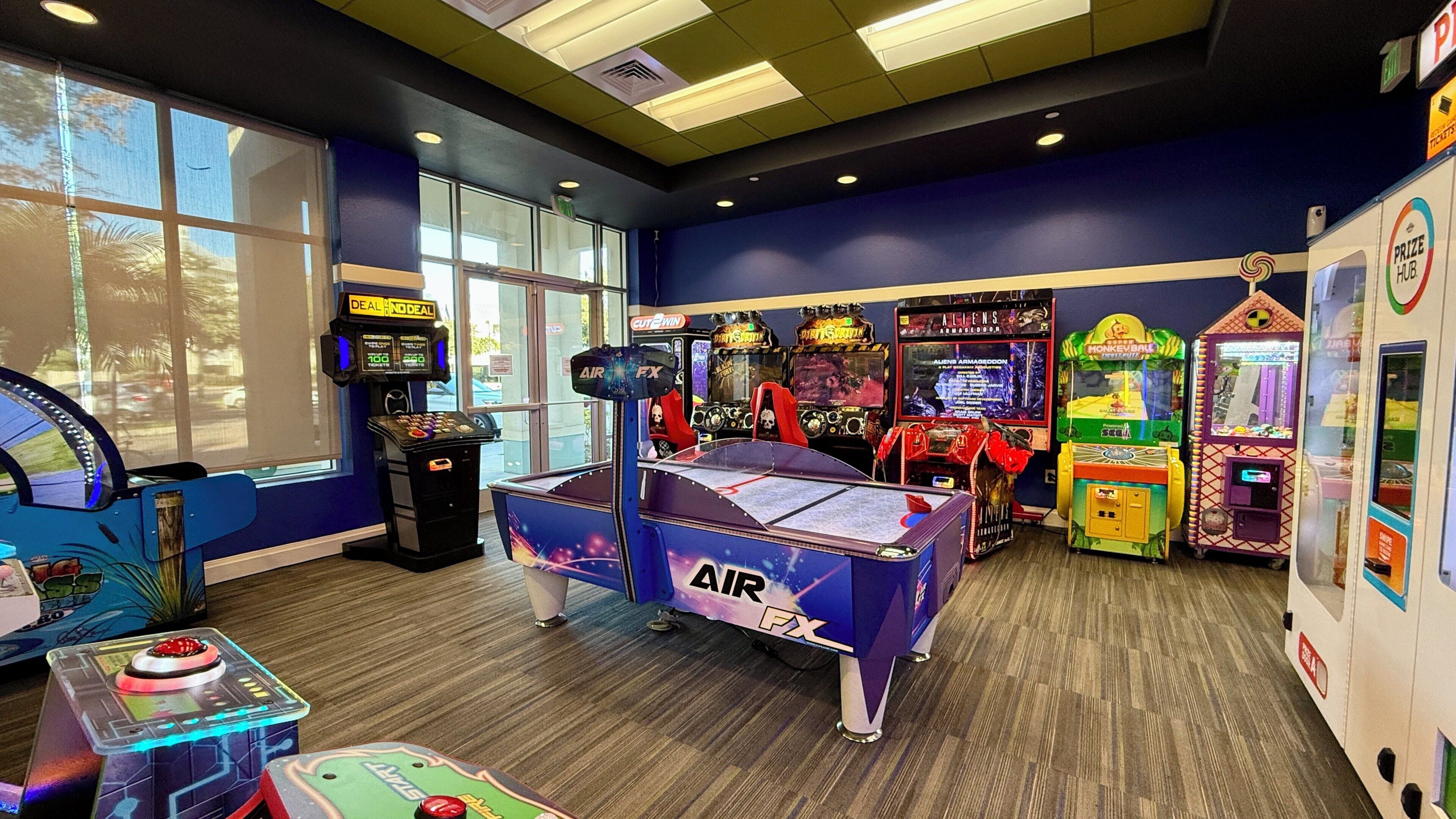 An indoor arcade with various gaming machines, including air hockey and claw machines, and a pool table.