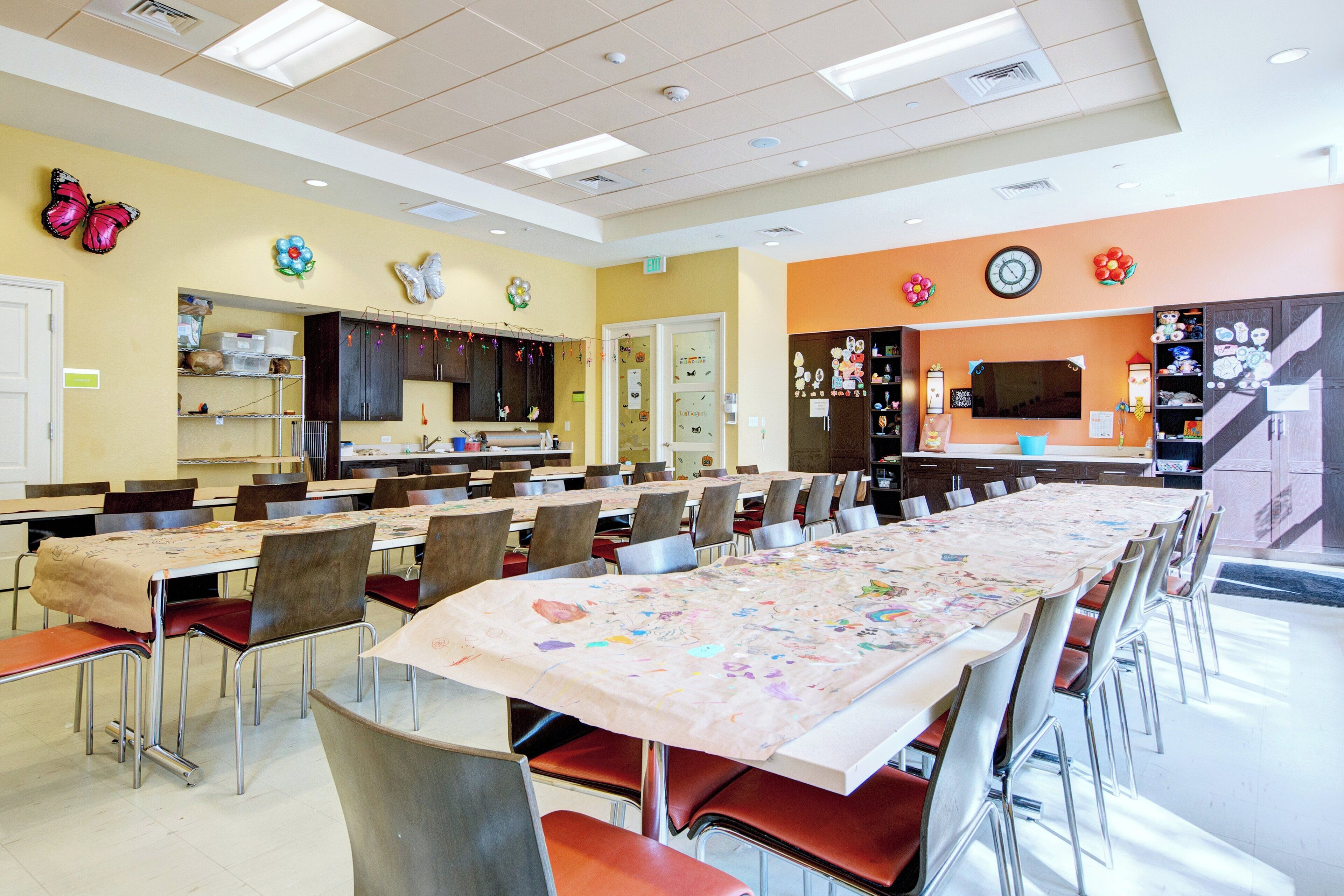 A dining hall with multiple tables and chairs, a kitchen area, and decorative wall elements.
