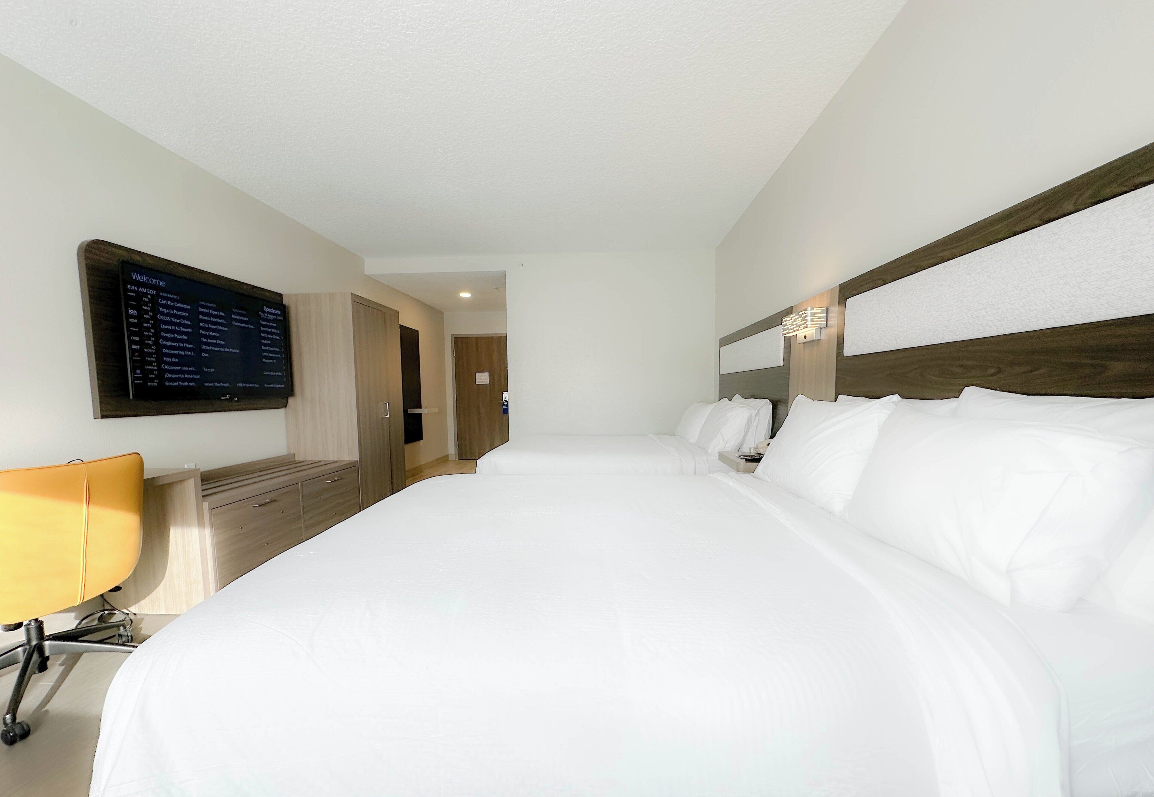 Habitación de hotel con cama, escritorio, silla, televisión y cabecero de madera.
