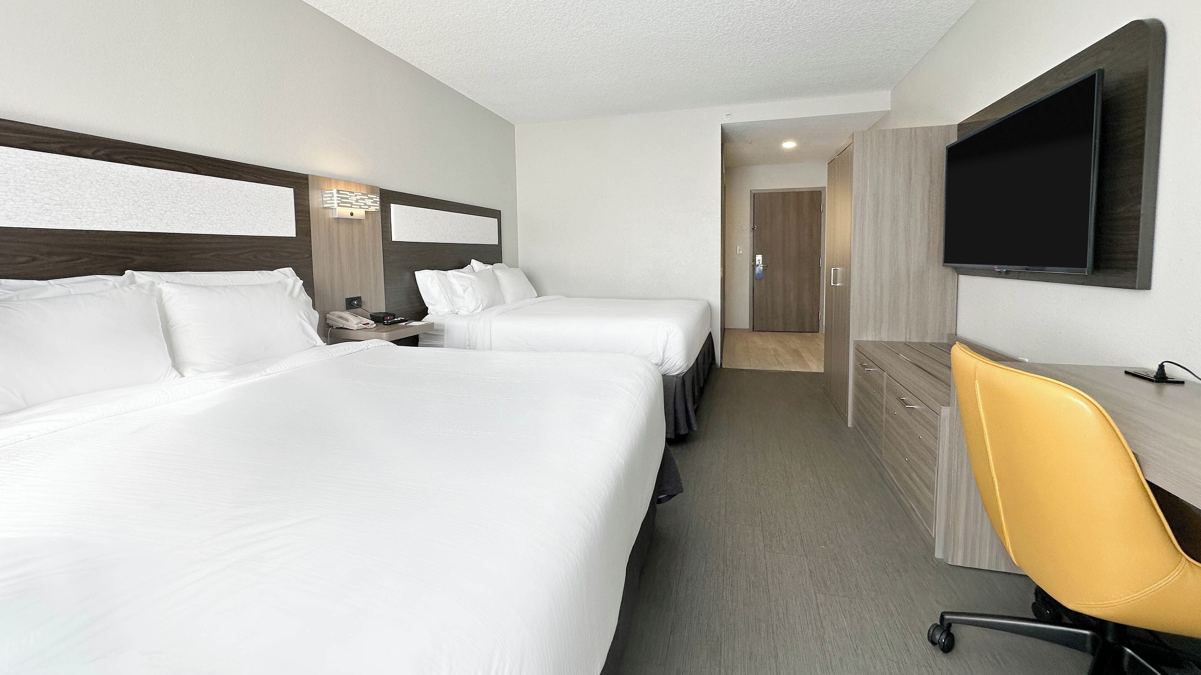 A hotel room with two beds, a desk, a chair, a TV, and a door leading to a bathroom.