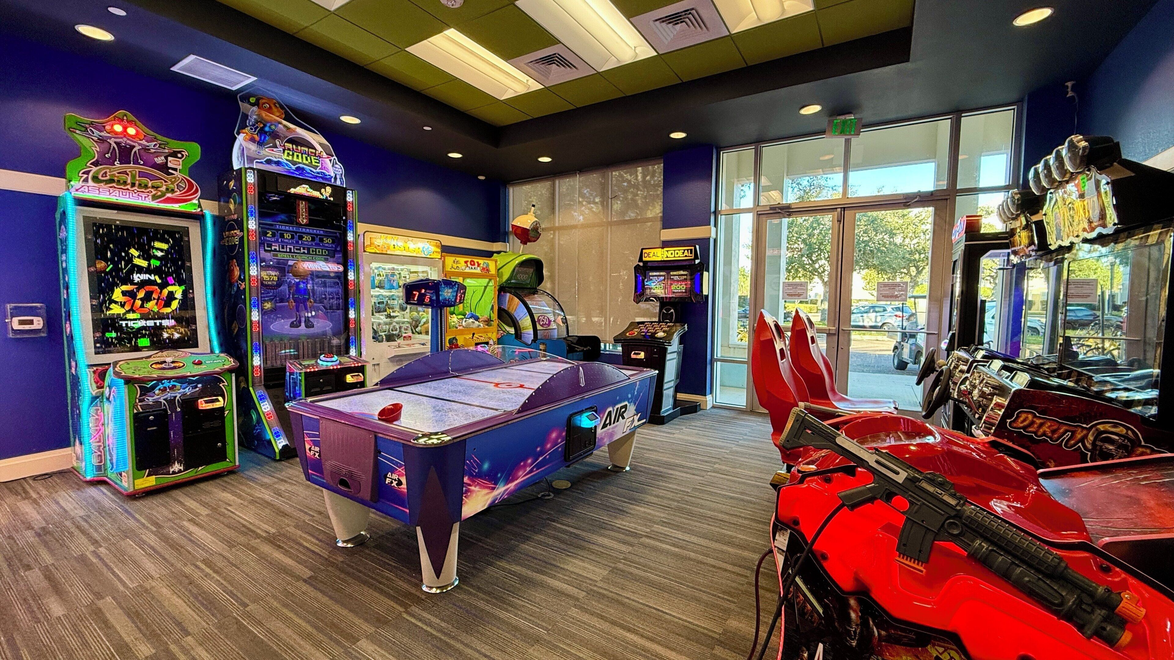 Un salón de juegos con varias máquinas, incluyendo una mesa de billar y un juego de carreras.