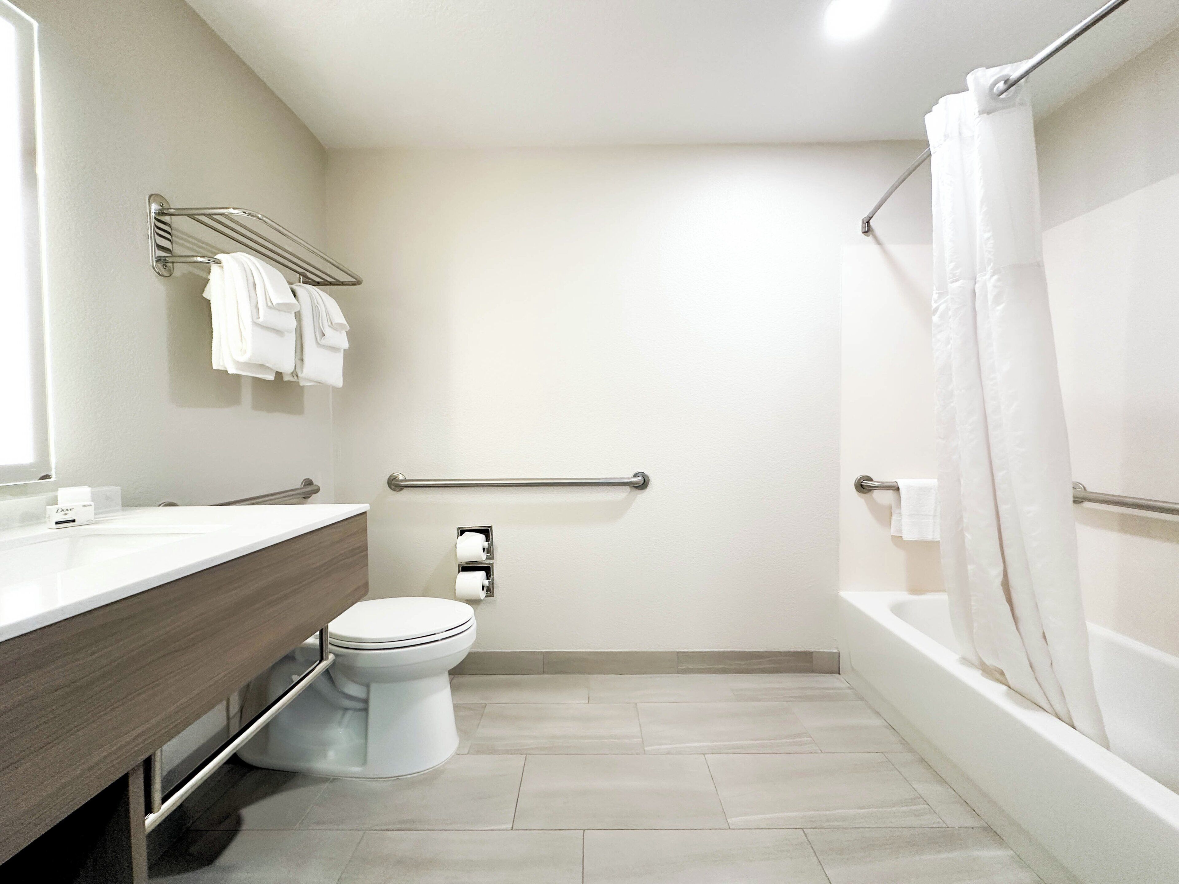 A modern bathroom with a toilet, a shower with a curtain, a vanity with a mirror, and a towel rack.