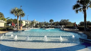 Una gran piscina al aire libre con una fuente en el centro, rodeada de palmeras y tumbonas.