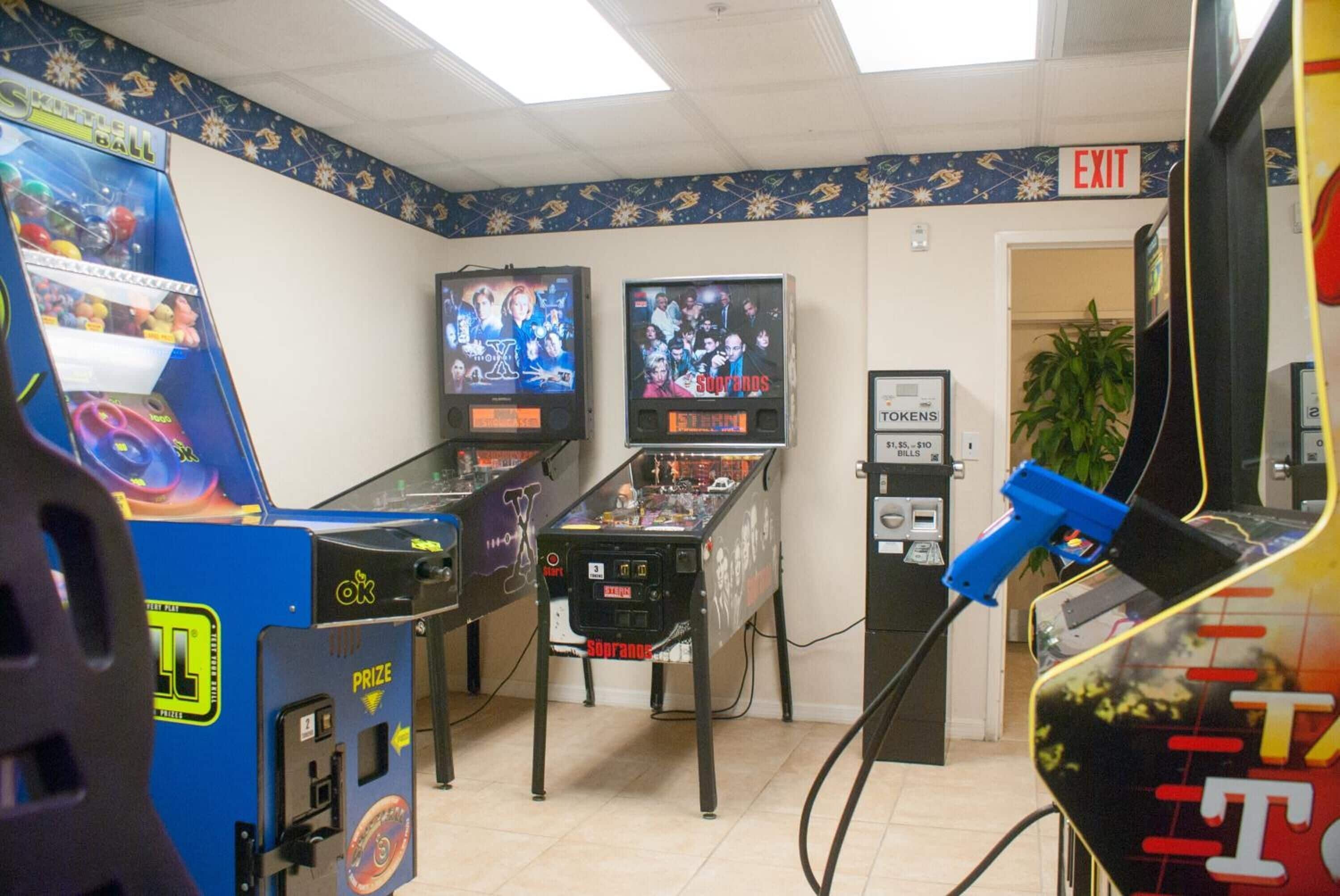 A room with arcade games, a sign for 'EXIT', and a 'TOKENS' machine.