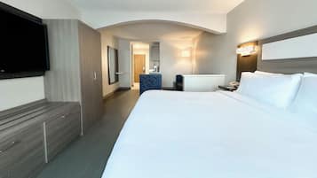 A hotel room with a large bed, a desk, a chair, a TV mounted on the wall, and a bathroom visible through an archway.