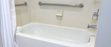 Una bañera blanca estándar con una barra de apoyo, una toalla blanca y una cortina de ducha.