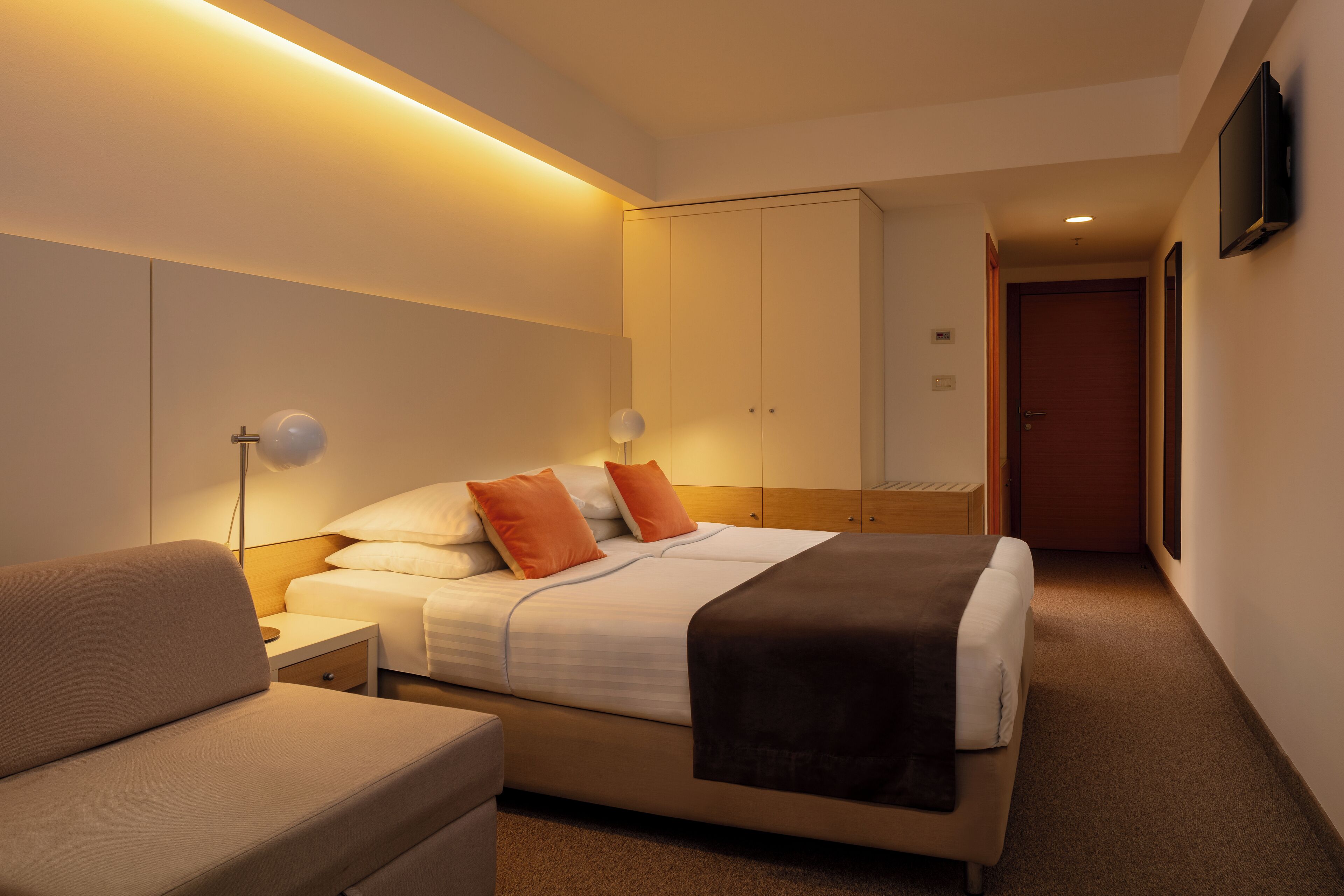 Une chambre d’hôtel moderne équipée d’un lit, de tables de chevet, d’un canapé et d’un téléviseur fixé au mur.