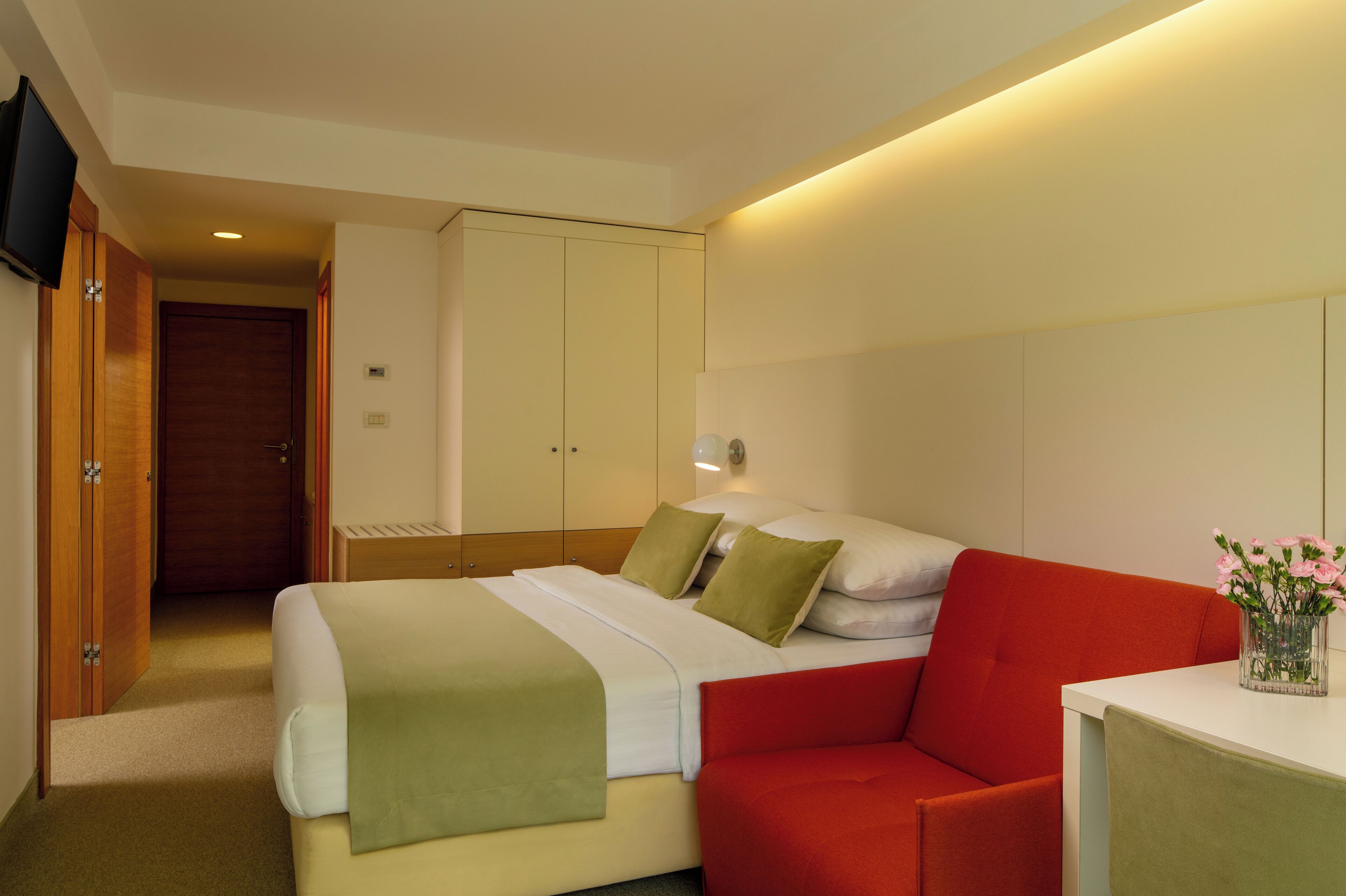 Habitació d'hotel amb un llit, un sofà vermell, una taula i un televisor penjat a la paret.