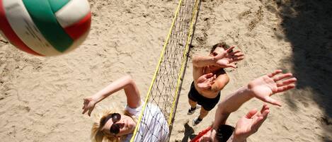 Un partido de voleibol de playa con jugadores extendiéndose para alcanzar la pelota.