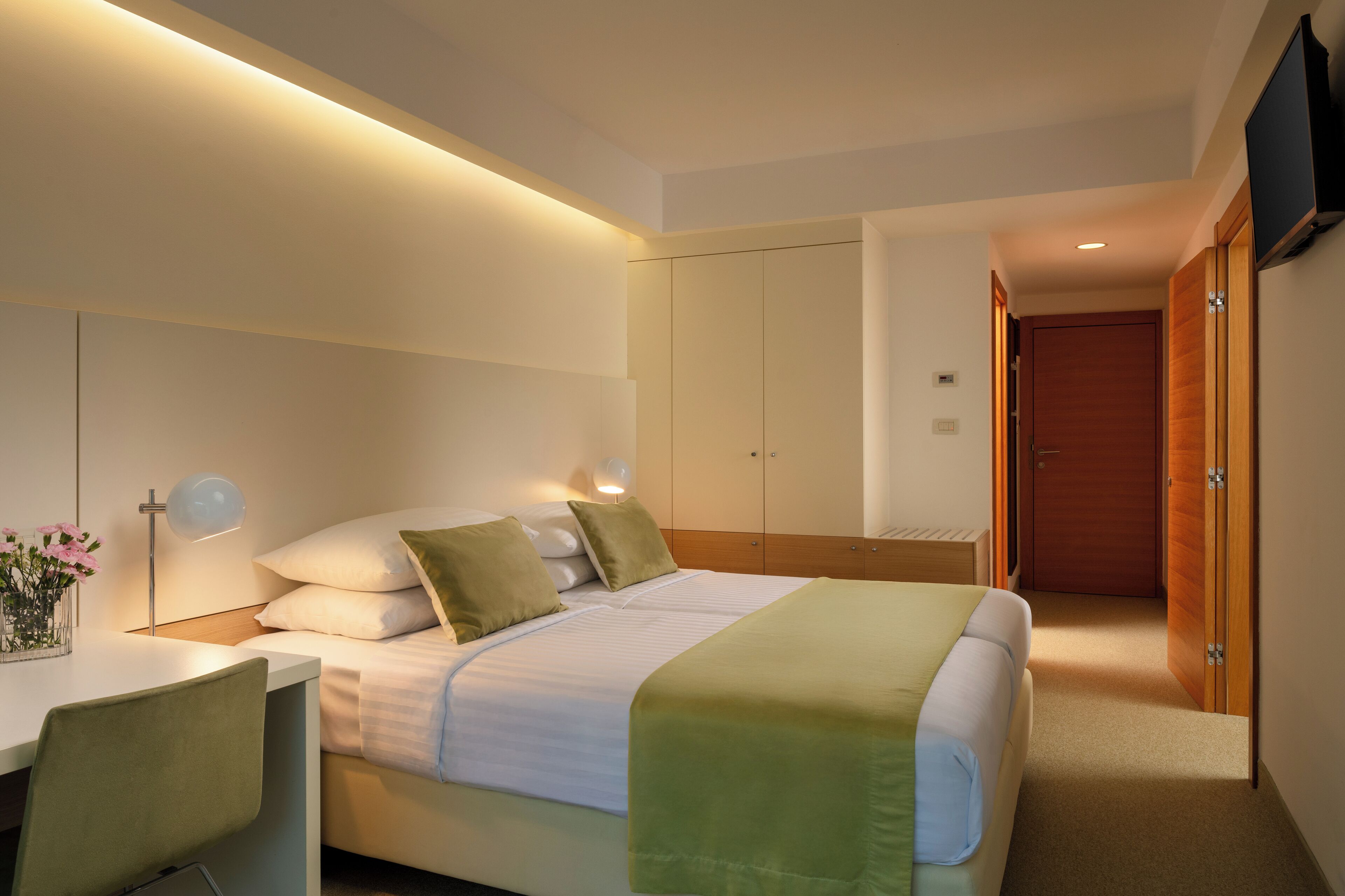 Ein Hotelzimmer mit Bett, Nachttisch, Lampe und einem an der Wand befestigten Fernseher.