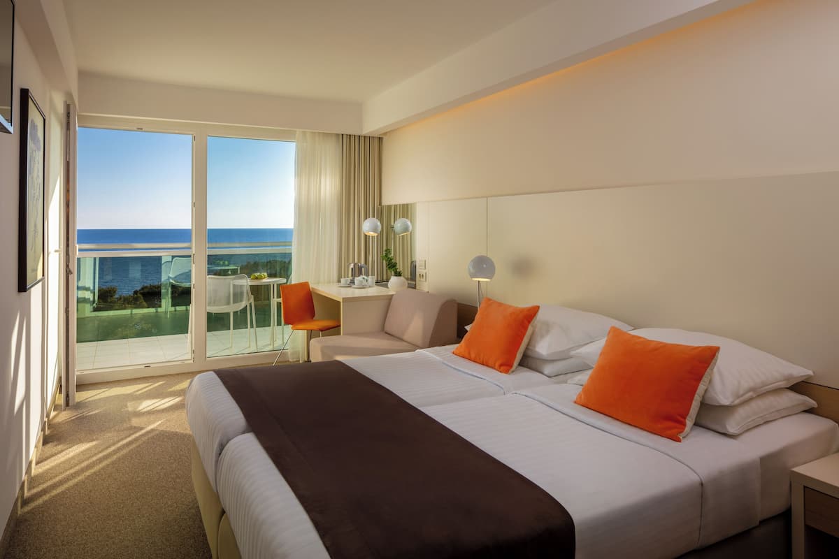 A hotel room with a bed, a desk, a chair, and a balcony with a view of the ocean.