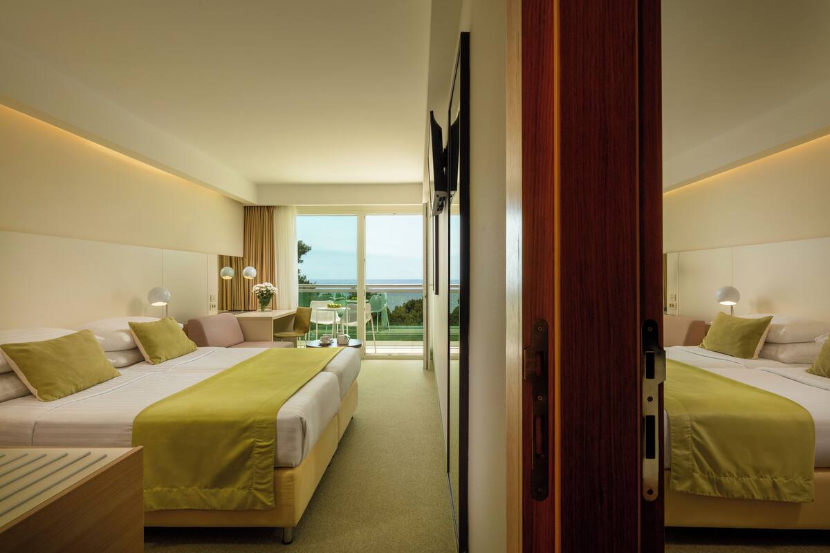 A hotel room with two beds, a balcony, and a view of the sea.