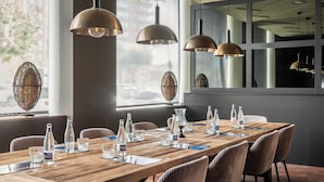 Un salón de conferencias con una larga mesa de madera, sillas, botellas de agua y jarrones decorativos.