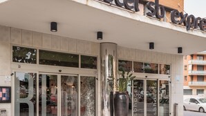 Entrada de hotel con puertas de cristal grandes, una planta en maceta y un letrero sobre la entrada.