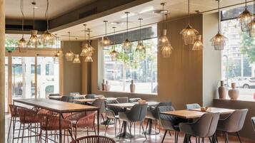 A spacious cafe with multiple tables and chairs, hanging pendant lights, and large windows offering views of the street.