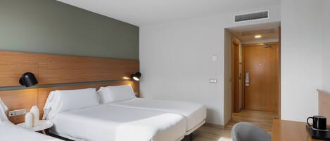 A hotel room with two beds, a desk, a chair, a lamp, and a door.