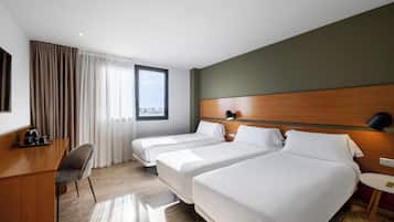 A hotel room with two beds, a desk with a chair, a small table, and a window with curtains.