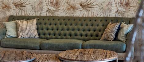 A green sofa with a tufted design, a round coffee table, and a wall with a 'Born to travel' sign.