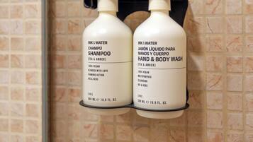 Dos botellas de champú y gel de baño en un soporte fijado a la pared de un baño con paredes de azulejos.