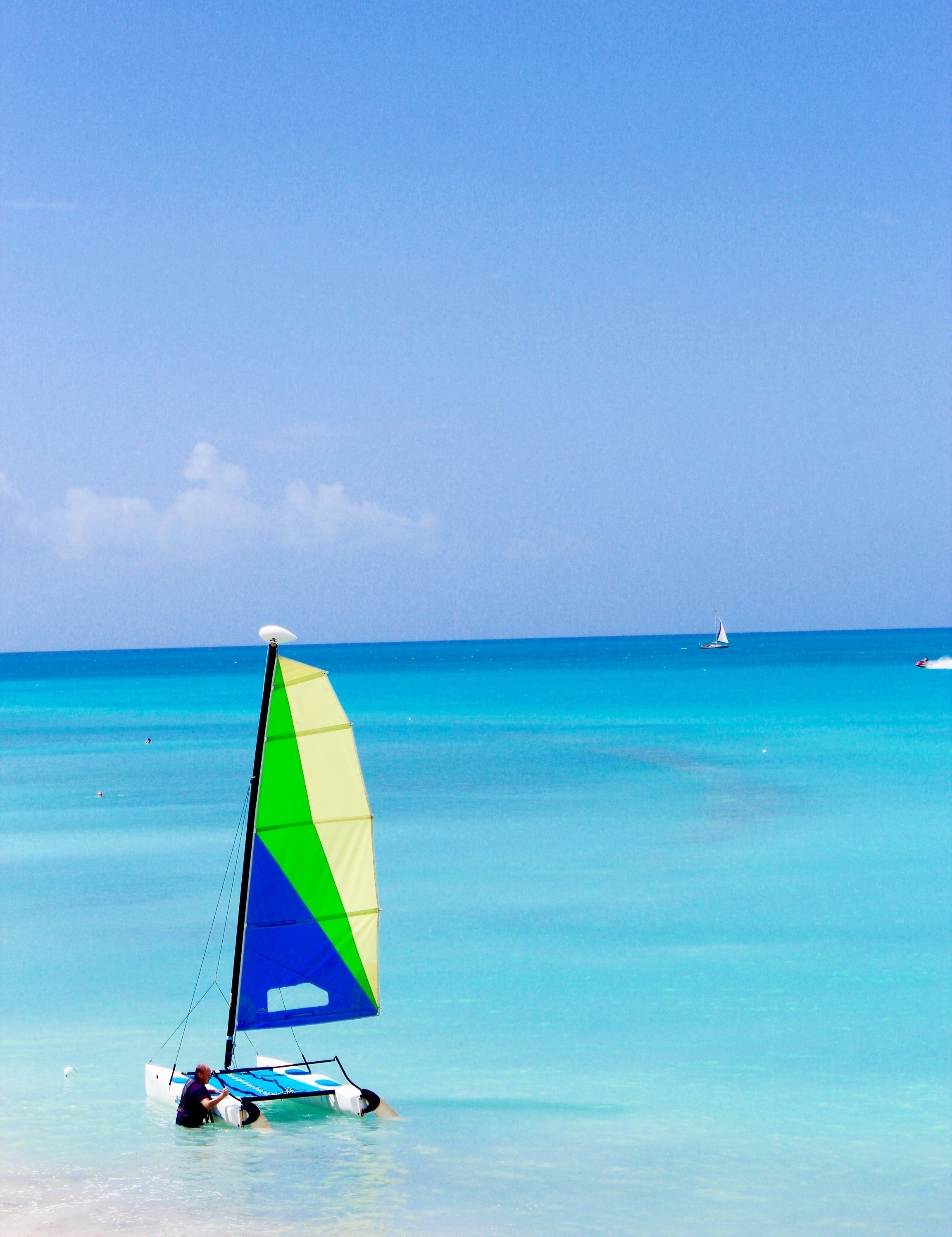 Un voilier aux voiles colorées naviguant sur des eaux turquoise et calmes.