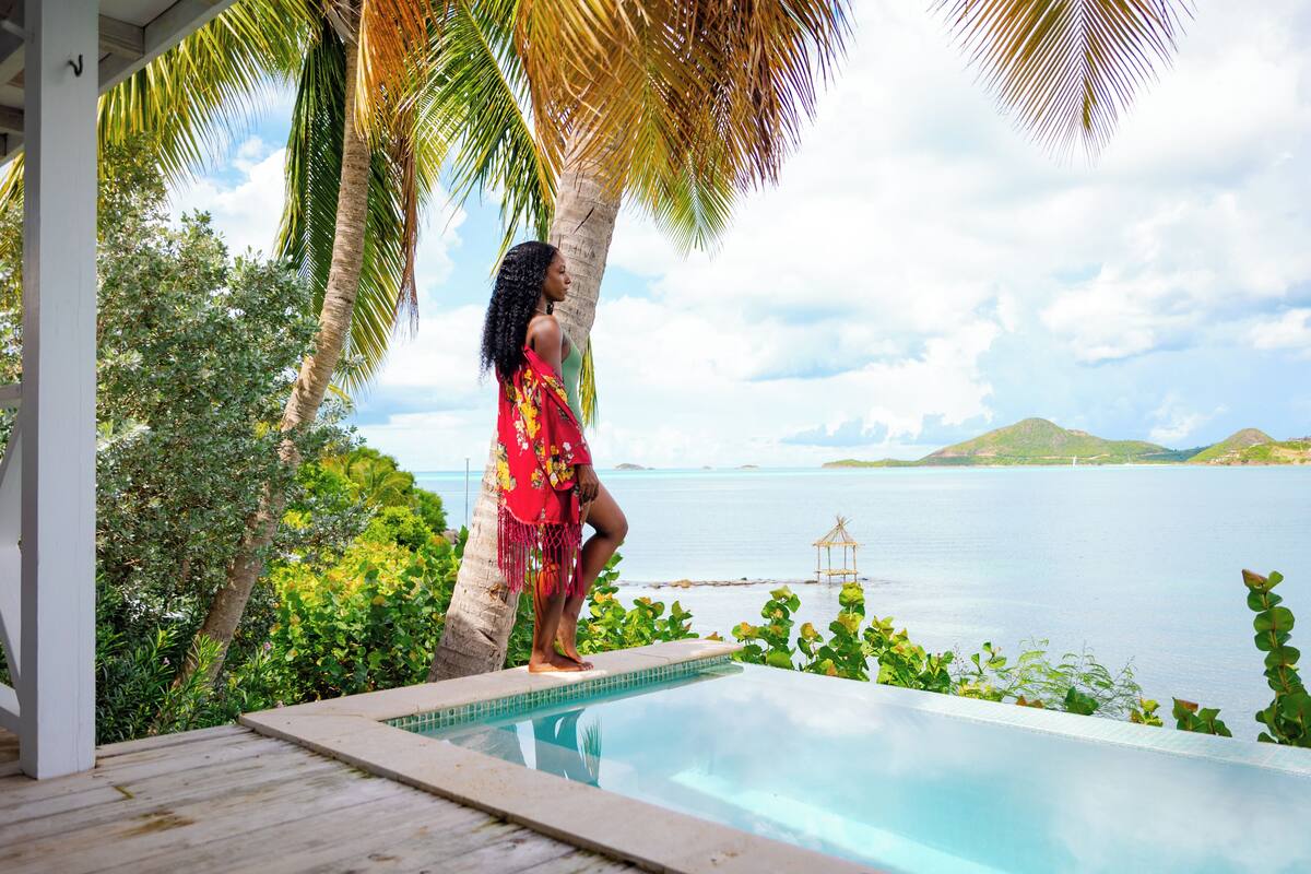 A person standing by a pool with a view of the sea and palm trees.