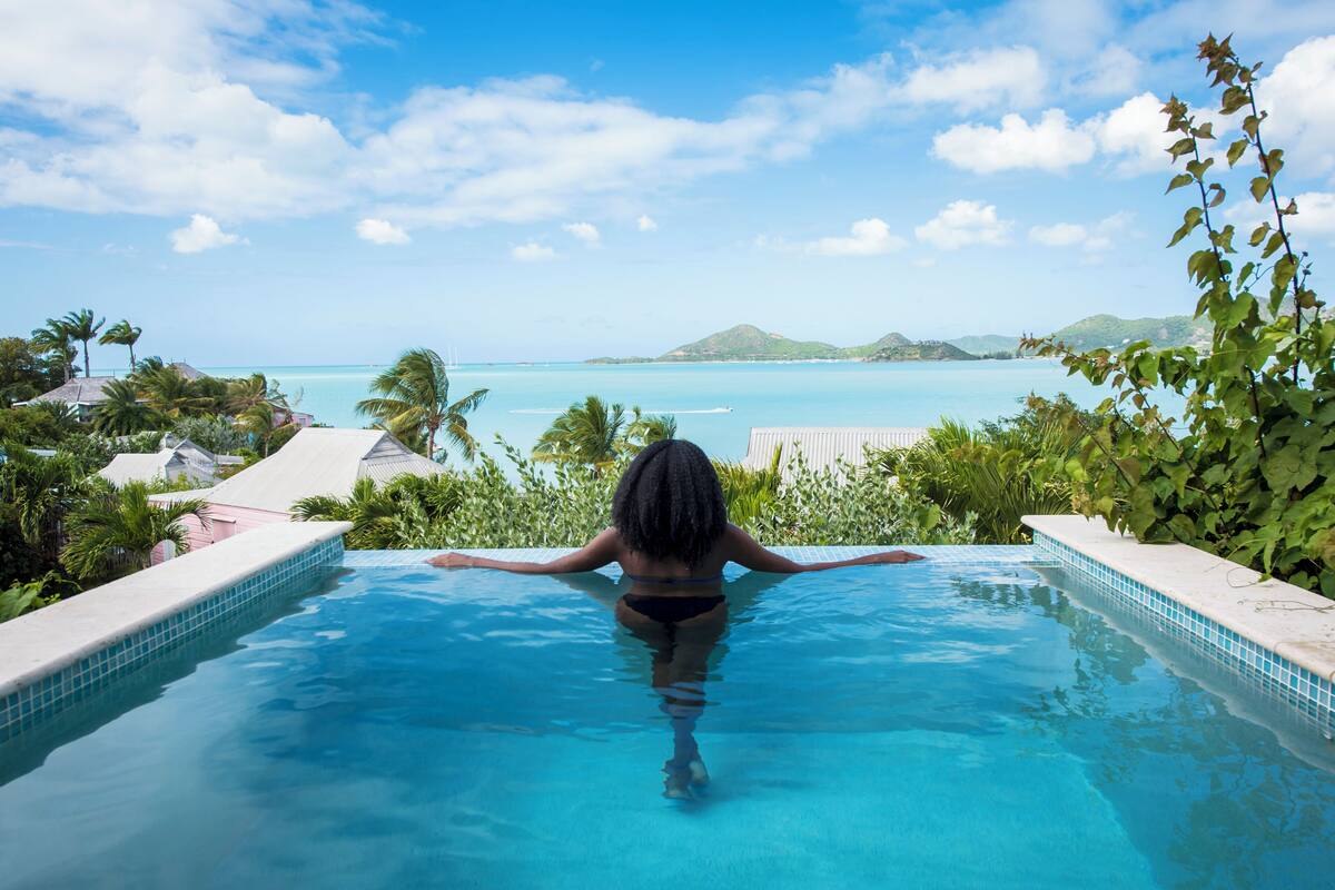 A woman in a swimming pool with a view of the ocean and hills.