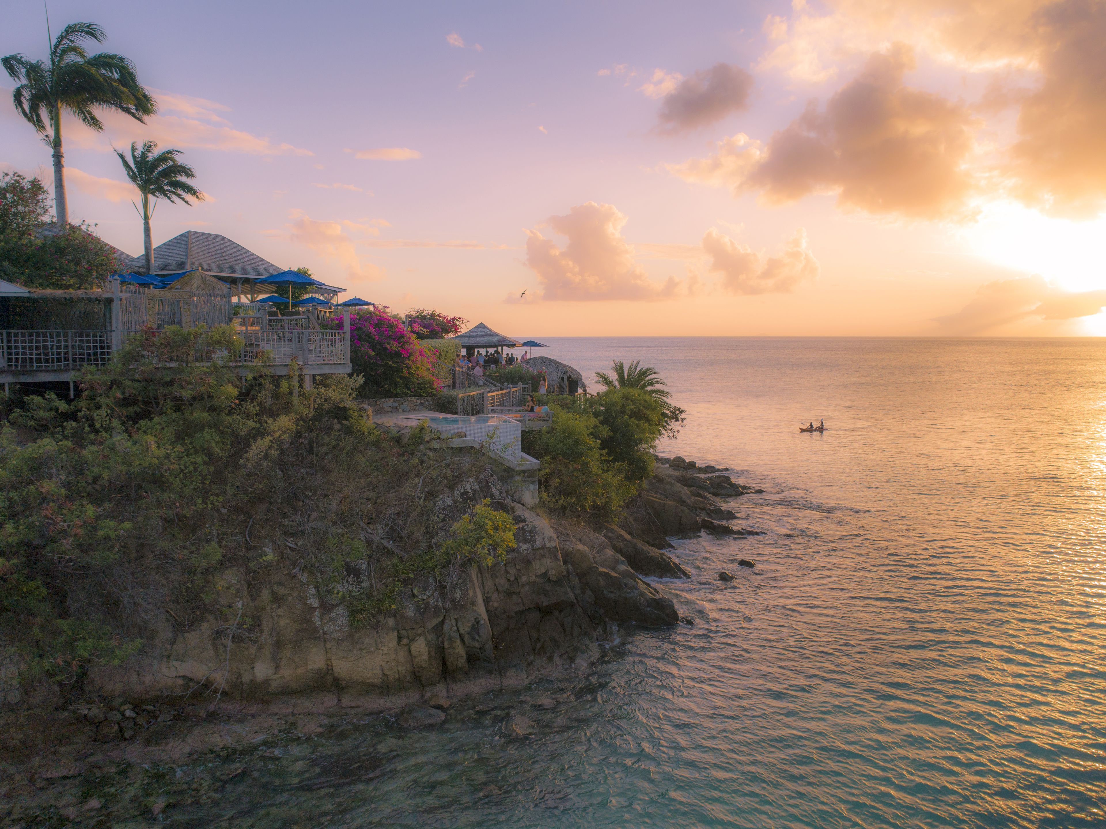 Ein Küstenresort mit Pool, Palmen und Blick auf das Meer bei Sonnenuntergang.