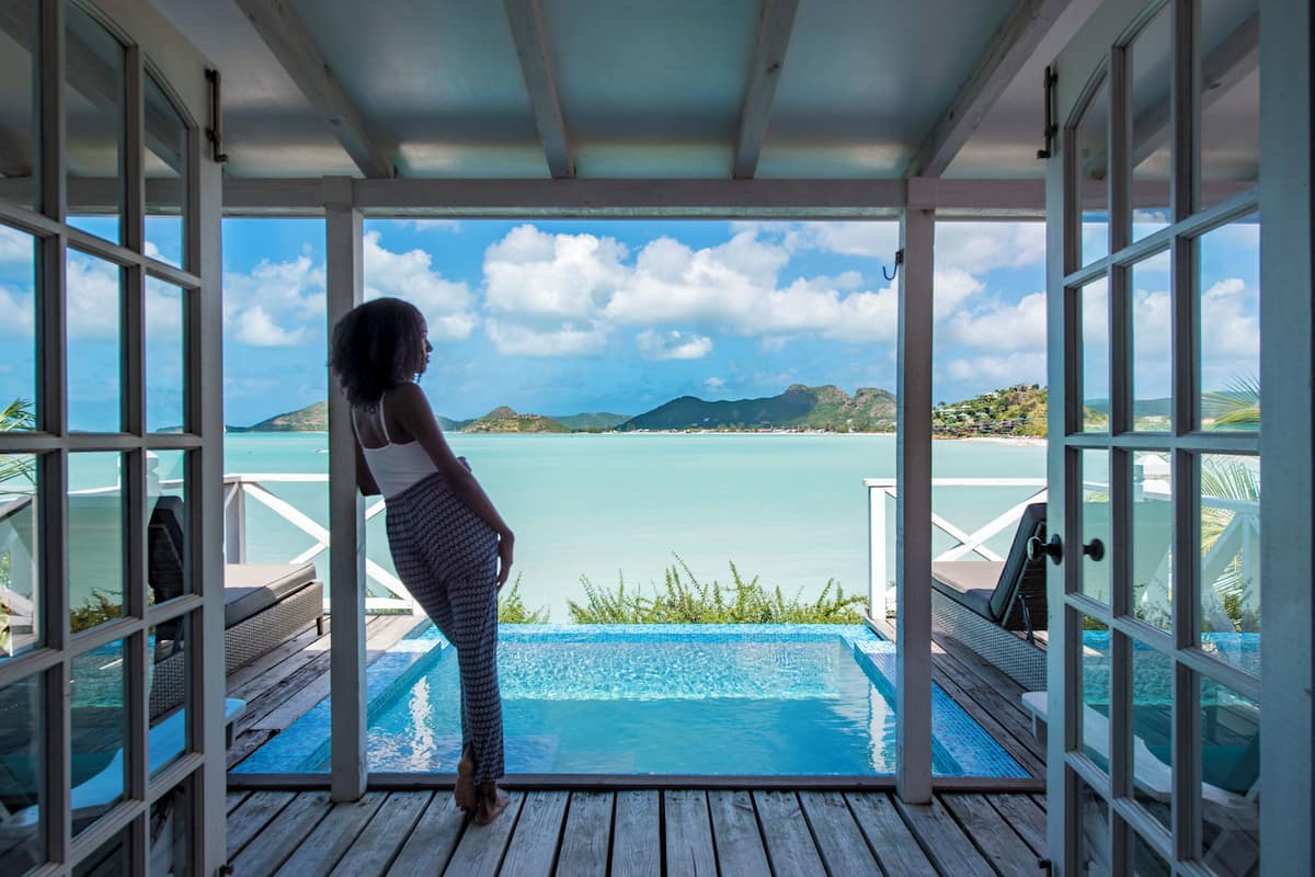 A person standing by a pool with a view of the ocean and hills.