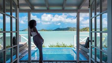 Eine Person steht am Pool mit Blick auf das Meer und die Hügel.