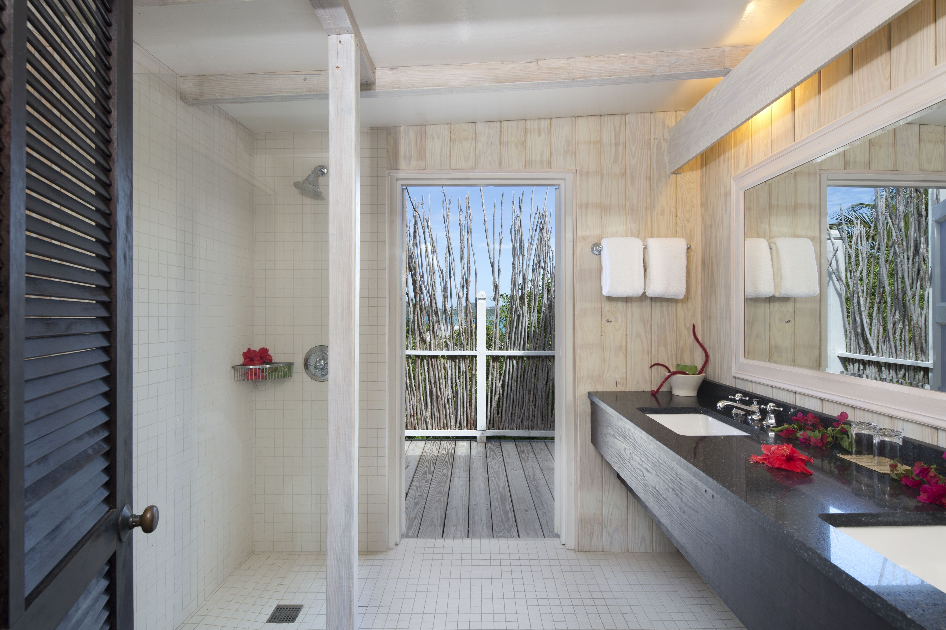 A bathroom with a wooden vanity, two sinks, a large mirror, and a shower area with a view of the outdoors.